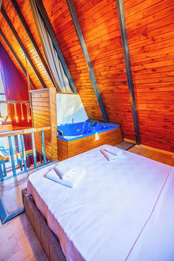 A room with a sloped ceiling, a bed, a wooden desk, and a blue bathtub.
