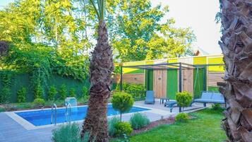 Una piscina con muelle de madera, rodeada de palmeras y césped verde.