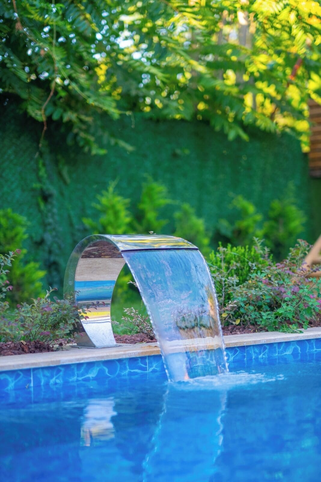 Un élément décoratif aquatique à l’eau claire, avec une structure métallique incurvée au centre d’un bassin, le tout entouré de verdure.