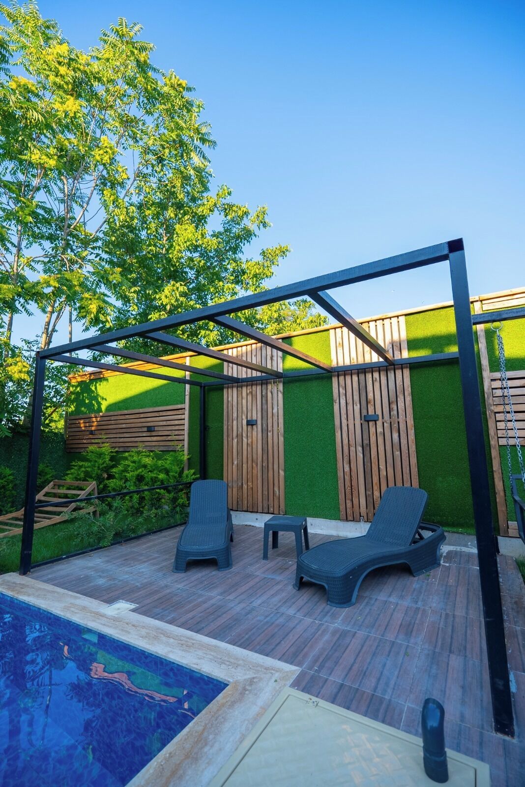 A covered outdoor area with a pool, two lounge chairs, and a wooden deck.