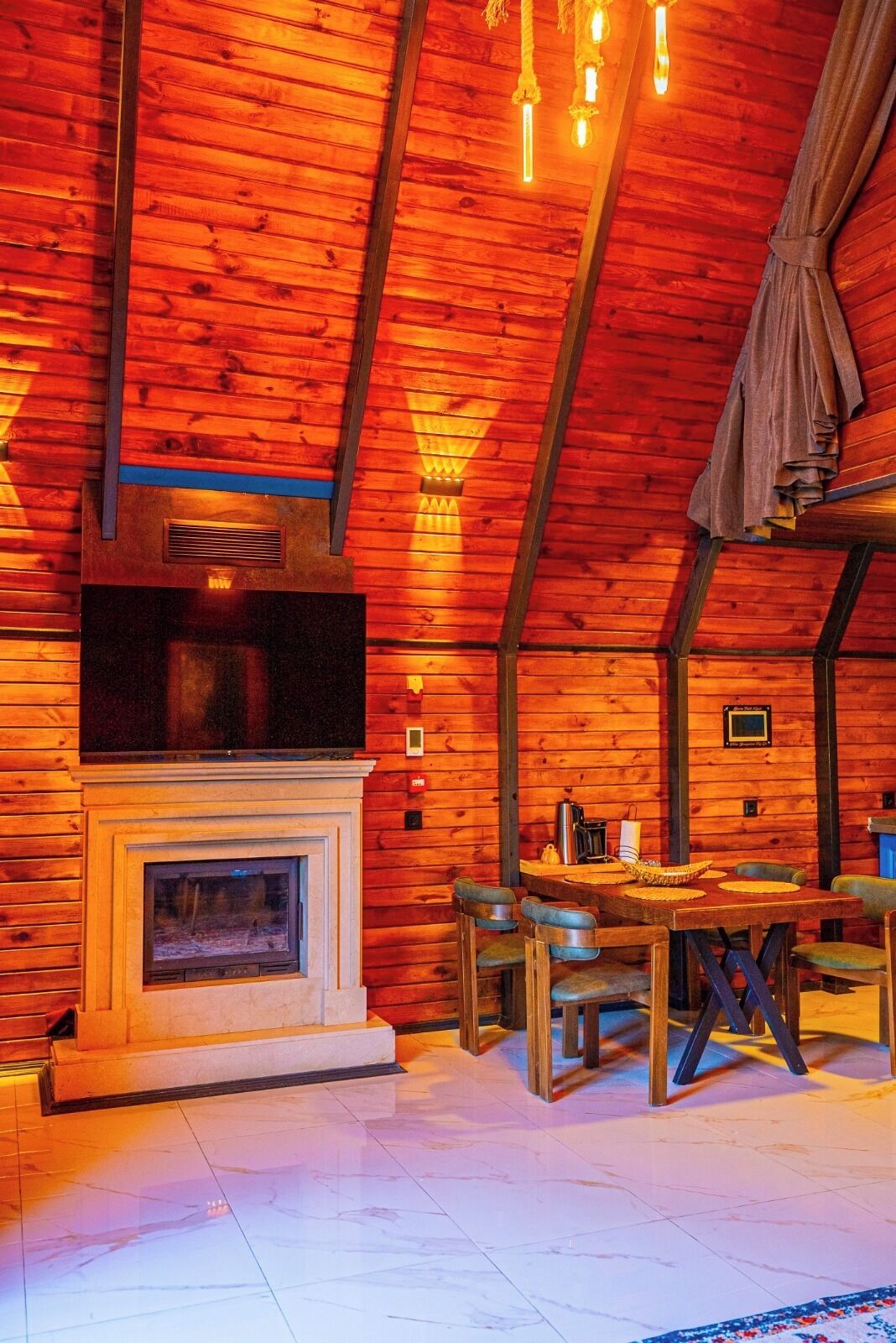A cozy cabin interior with a fireplace, wooden walls, and a dining area.