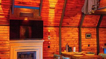 A cozy cabin interior with a fireplace, wooden walls, and a dining area.
