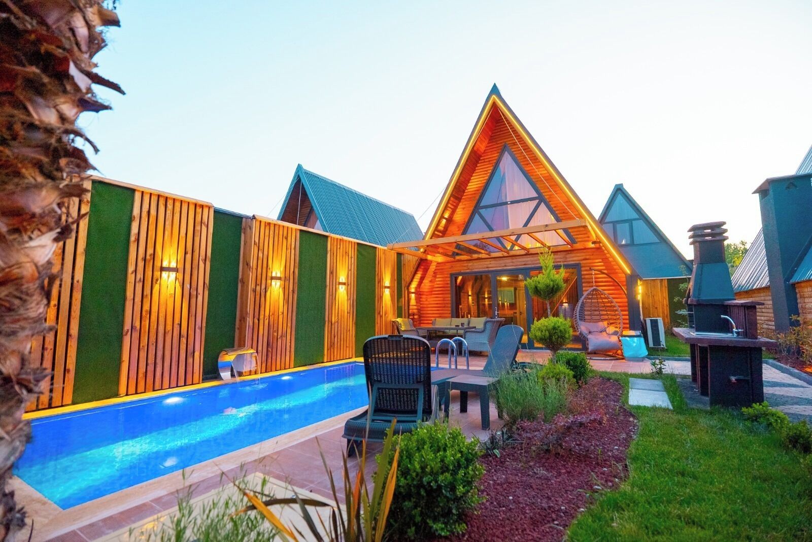 A modern log cabin with a swimming pool, outdoor seating, and a barbecue area.