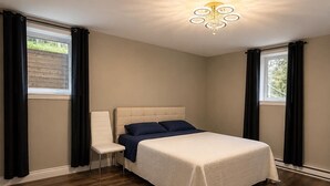 A bedroom with a bed, a chair, a chandelier, and large windows with curtains.