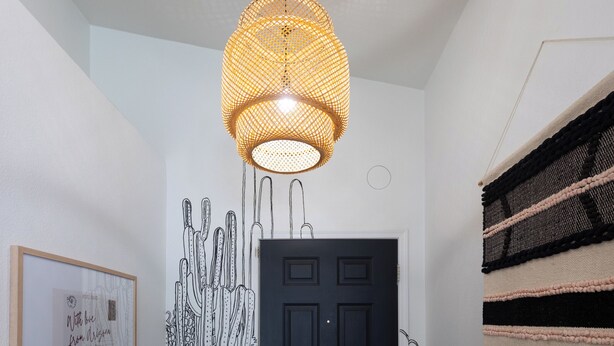 En gang med en sort dør, en vægmonteret lampe, et indrammet billede og en vægkunst med struktur.