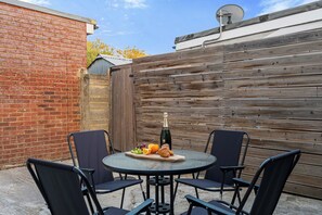 A round outdoor table with four chairs, a bottle of champagne, and a plate of fruit and croissants. - Family & Contractor Stay | Sleep 7 |NR Heathrow (Langley)