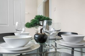 A dining table set with white bowls, plates, and wine glasses, centered around a bonsai tree in a black vase. - Family & Contractor Stay | Sleep 7 |NR Heathrow (Langley)
