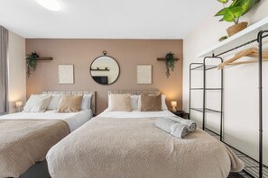 A hotel room with two beds, a round mirror, wall art, a plant, and a metal rack. - Family & Contractor Stay | Sleep 7 |NR Heathrow (Langley)