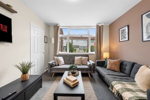 A modern living room with a sofa, a coffee table, and a TV mounted on the wall. - Family & Contractor Stay | Sleep 7 |NR Heathrow (Langley)
