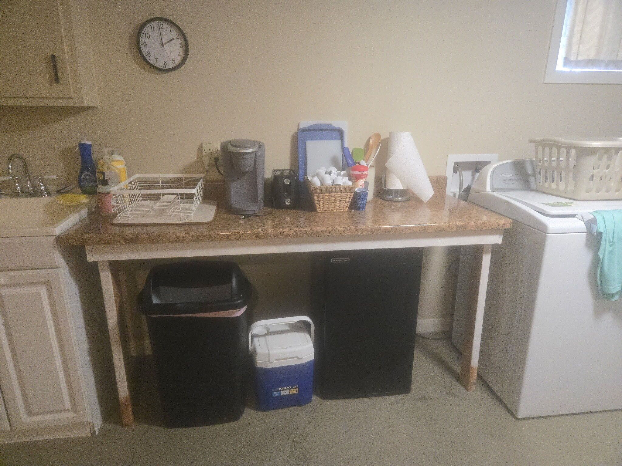 A kitchen with a sink, coffee maker, and a clock on the wall.