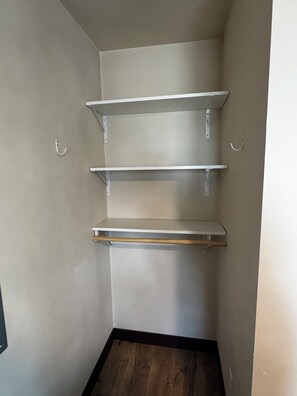 A corner with three white shelves against a wall, a dark wooden floor, and a white door. - Private, quiet cabin in the trees with farm experience! (Rapid City)