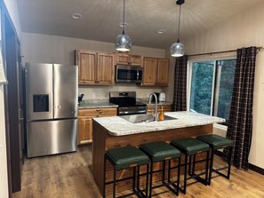 A modern kitchen with wooden cabinets, stainless steel appliances, a granite countertop, and a bar stool area. - Private, quiet cabin in the trees with farm experience! (Rapid City)