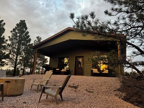 A cabin with a covered porch, two Adirondack chairs, and a table. - Private, quiet cabin in the trees with farm experience! (Rapid City)