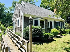 Ein Haus mit überdachter Veranda, einer Holzterrasse und einem Garten mit verschiedenen Pflanzen.