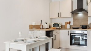 A modern kitchen with white cabinetry, a built-in oven, and a dining table set for four. - Stylish 2-Bed Flat, Leyland – Near Worden Park (Lancashire)