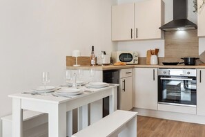A modern kitchen with white cabinetry, a built-in oven, and a dining table set for four. - Stylish 2-Bed Flat, Leyland – Near Worden Park (Lancashire)