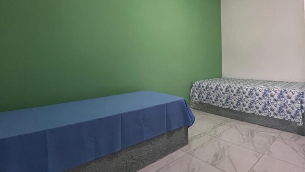 A room with a blue bed and a patterned bedspread, a green wall, and a white wall.