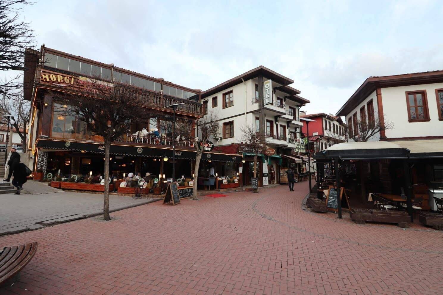 A street with a restaurant named 'MORGI' and a hotel with a balcony.
