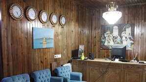 Una habitación con paneles de madera, un candelabro, un cuadro, un escritorio con una computadora y tres sillones tapizados en azul.