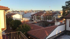 A residential area with terracotta-tiled roofs, a courtyard with a staircase, and a view of the cityscape in the background. - Özkonak Hotel (Ankara)