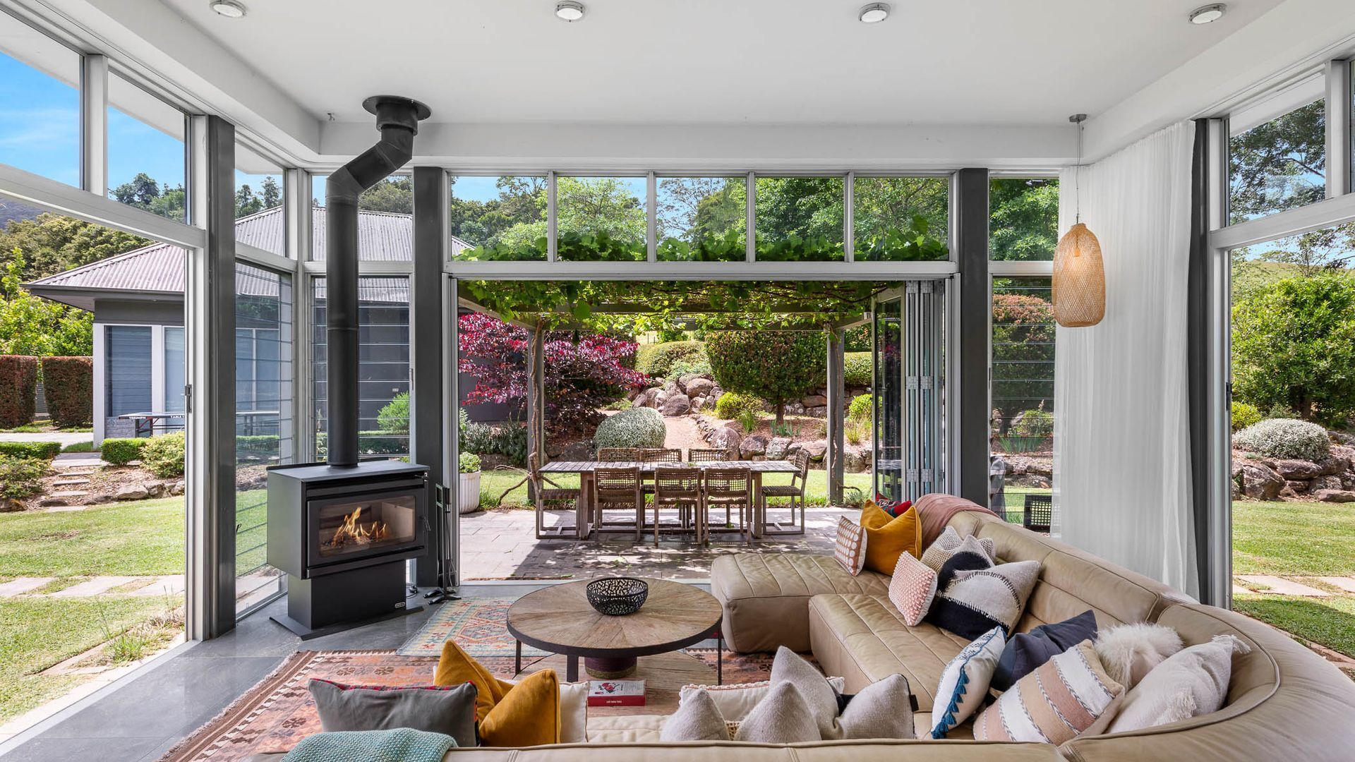 A modern interior with a fireplace, a sofa, and a dining area with a view of a garden.