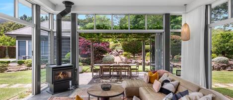 A modern interior with a fireplace, a sofa, and a dining area with a view of a garden.