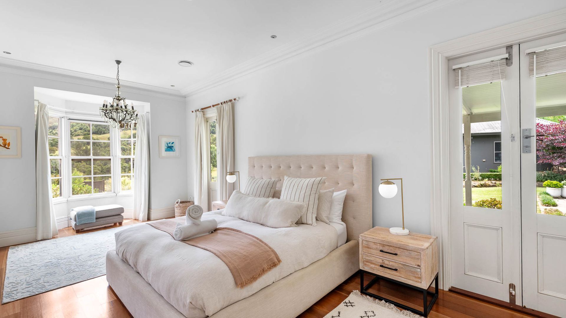 Une chambre à coucher avec un grand lit, des tables de chevet, un lustre et une vue sur l’extérieur.