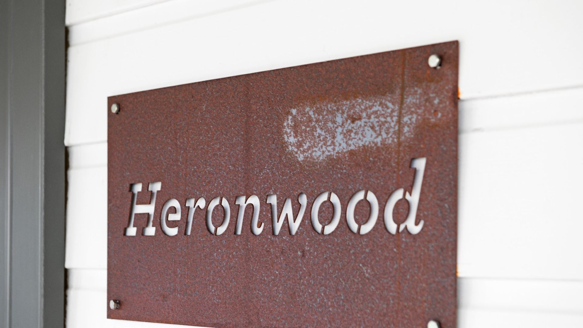 Una señal metálica con el nombre 'Heronwood' colocada en una pared.