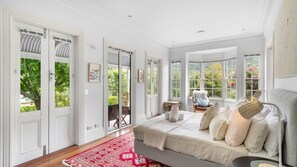 A bedroom with a large bed, a red patterned rug, and a view of greenery through the windows. - Heronwood - Luxury Country Retreat (Wattamolla)