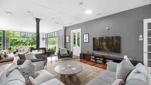 A modern living room with a fireplace, comfortable seating, a large flat-screen TV, and a bookshelf. - Heronwood - Luxury Country Retreat (Wattamolla)