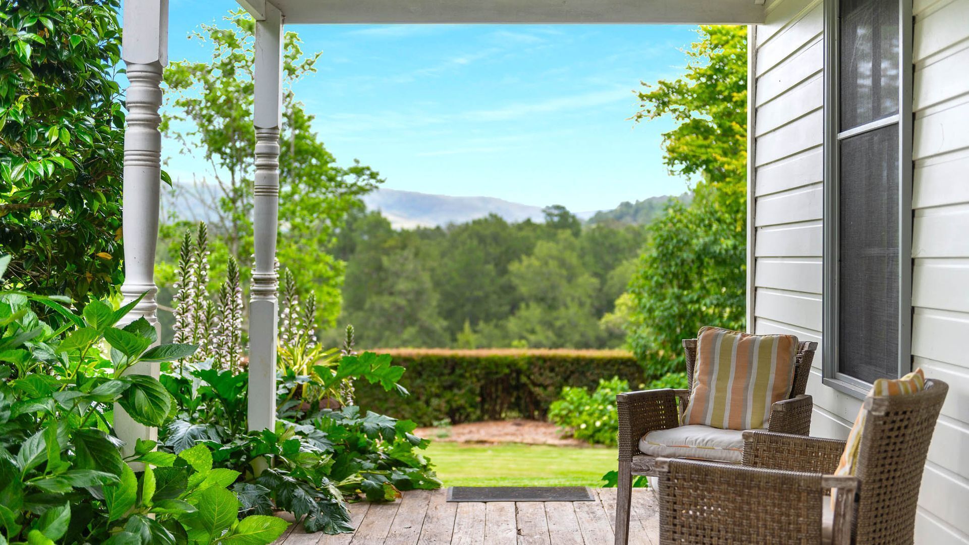 A porch with wicker furniture and a view of a green landscape.