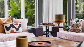 Ein modernes Wohnzimmer mit einer Sofagarnitur, einem kleinen Tisch mit Dekoration und Blick ins Grüne durch große Fenster.