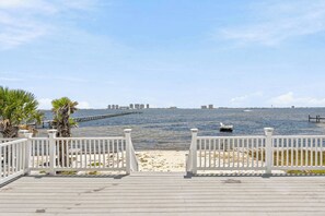 A wooden deck with white railings overlooking a calm body of water, a distant city skyline, and a clear sky. - Waterfront Views & Beach Access - Pet Friendly! (Navarre)