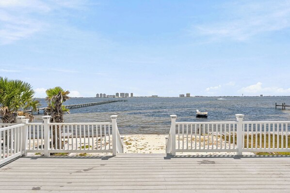 A wooden deck with white railings overlooking a calm body of water, a distant city skyline, and a clear sky. - Waterfront Views & Beach Access - Pet Friendly! (Navarre)