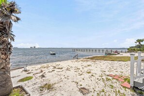 A beach with a palm tree, a boat, and a pier extending into the water.