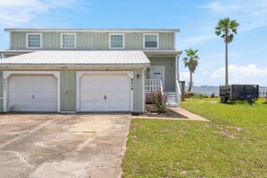 A two-story house with a garage, a small porch, and a view of the water.