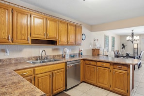 A kitchen with wooden cabinets, a stainless steel dishwasher, granite countertops, and a dining area with a chandelier.