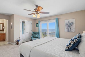 Une chambre à coucher avec un lit, une chaise, un ventilateur de plafond et une vue sur l’océan par la fenêtre.