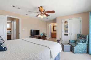 A bedroom with a bed, a television, a ceiling fan, and a door leading to a bathroom.