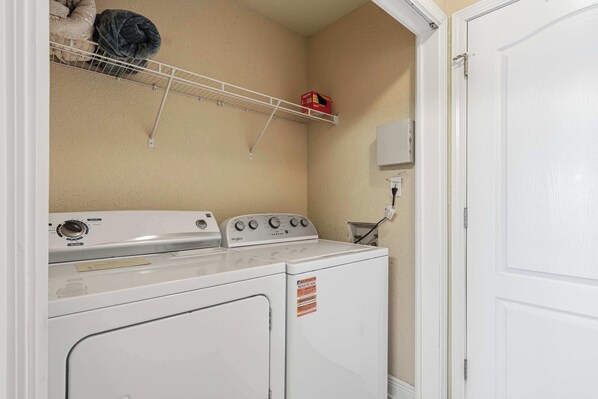 A laundry room with a stacked washer and dryer, a shelf with a blanket, and a wall-mounted electrical outlet.