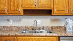 Una cucina con mobili in legno, un piano di lavoro in granito, un lavello a due vasche e una lavastoviglie.
