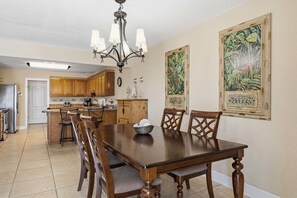 A dining area with a wooden table and chairs, a chandelier, and two framed botanical paintings on the wall.