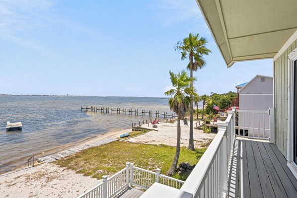 A beachfront property with a wooden deck, a sandy beach, and a view of the ocean.