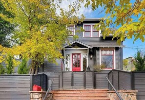 A two-story house with a red front door, a small porch, and a stone wall in front. - Historic Mapleton Hill House (Boulder)