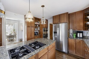 Cozinha com bancadas de granito, eletrodomésticos de aço inoxidável, armários de madeira e iluminação pendente.