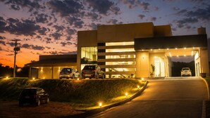 A modern building with a covered entrance, multiple cars parked in front, and a well-lit driveway. - Hotel Imperador (Gurupi)