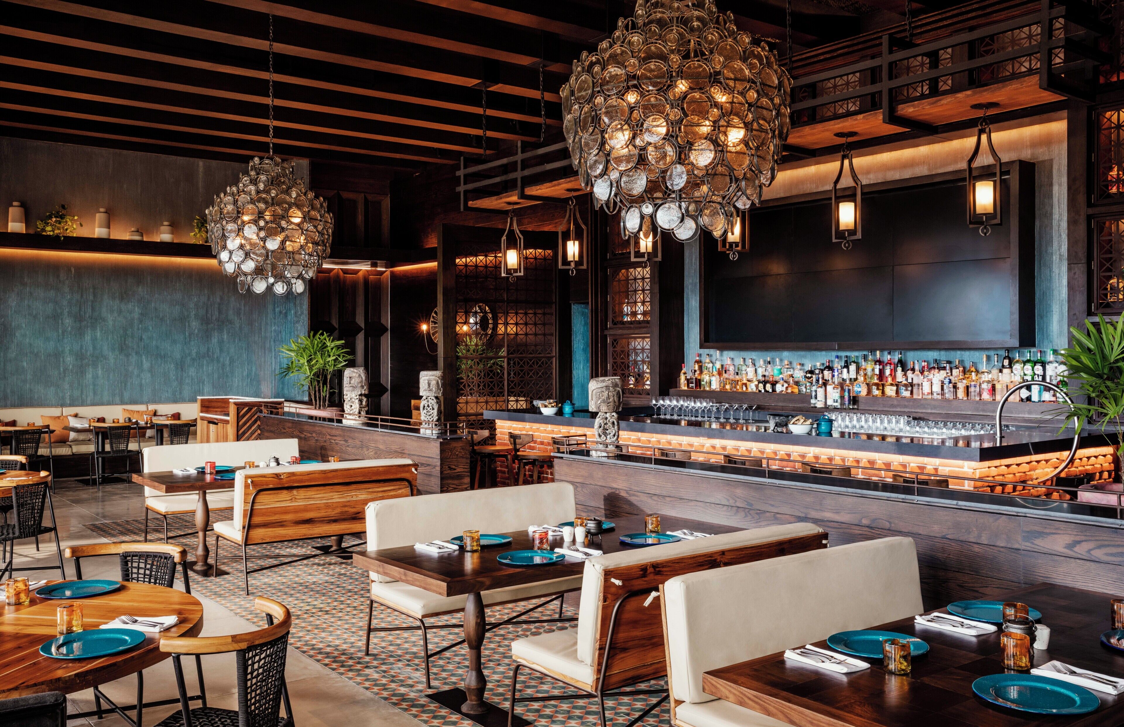 Un interior de restaurante con mesas y sillas de madera, una zona de bar y luminarias decorativas.