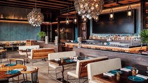 A restaurant interior with wooden tables, chairs, a bar area, and decorative lighting fixtures.