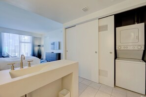 Una camera d'albergo con un letto grande, un bagno moderno con lavandino e specchio, una TV a schermo piatto e una lavatrice e asciugatrice integrate.