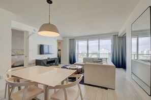 A modern living room with a dining area, a sofa, a TV, and large windows with a city view. - Cozy 2-bedroom Condo At W Residences Fort Lauderdale With Pool & Beach Service (Fort Lauderdale)